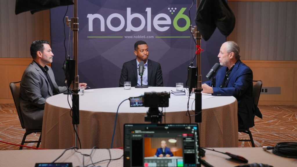 Three business professionals recording a roundtable podcast with professional video production lighting and Noble6 branded backdrop